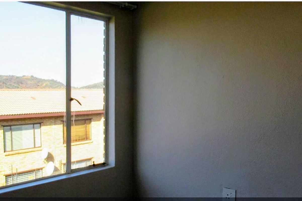 An empty bedroom featuring a large window with views of the surrounding residential complex.