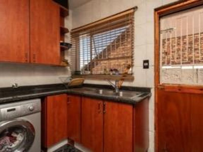 Functional scullery featuring timber cabinetry, granite countertops, stainless steel sink, and direct access to the exterior via a timber door.