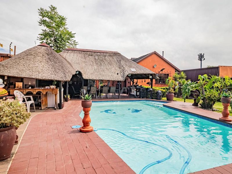 Outdoor entertainment area featuring a swimming pool, brick-paved surround, and a large thatched lapa with a built-in bar area.