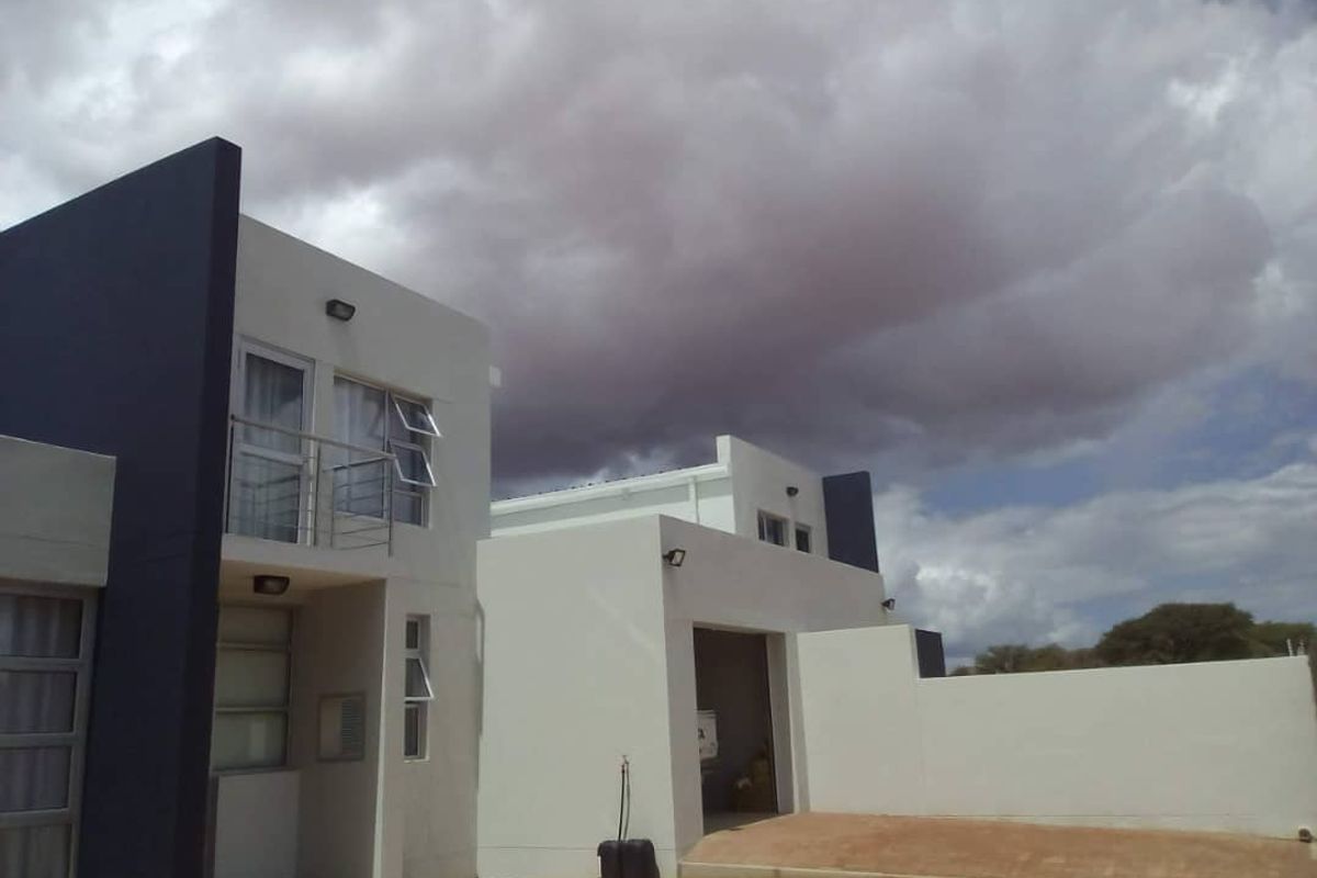 Modern two-story apartment exterior featuring a clean white and dark grey facade, balcony with stainless steel railing, and an integrated garage.