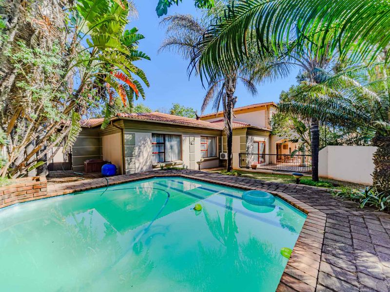 Outdoor pool area featuring a paved surround, established garden landscaping, and direct access to the rear of the residence.