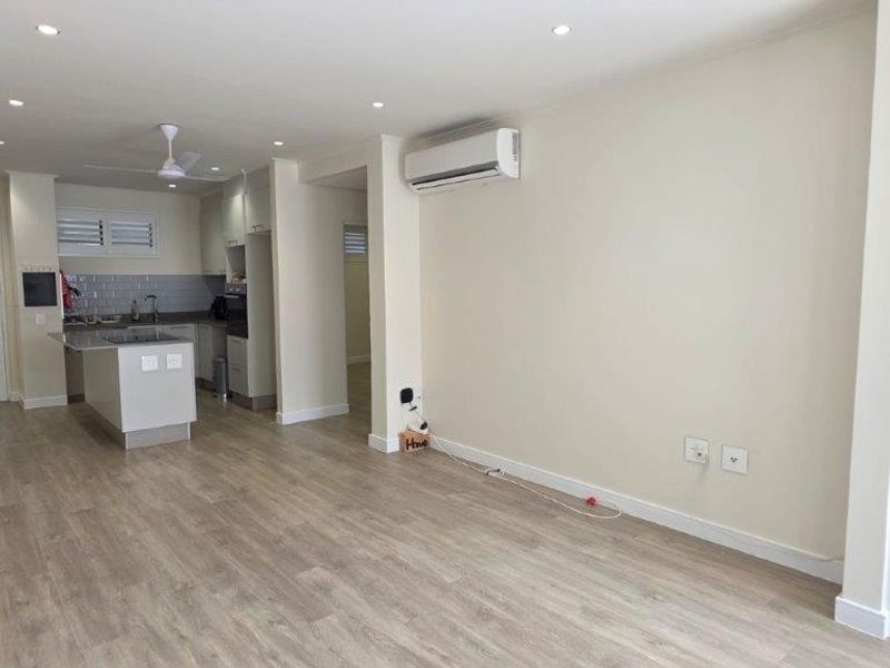 Spacious open-plan living area featuring modern laminate flooring, recessed lighting, a split-system air conditioner, and a functional kitchen with built-in appliances.