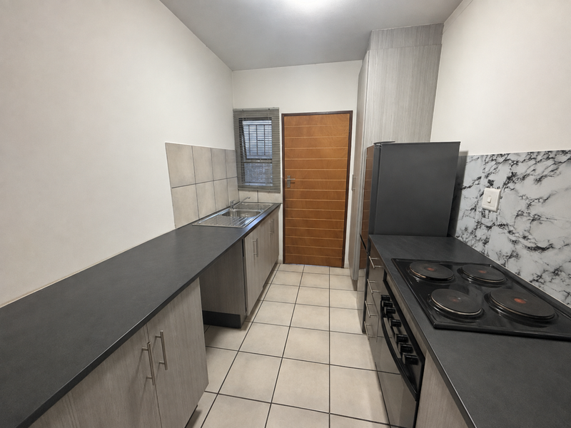 A functional galley-style kitchen featuring modern laminate countertops, built-in cabinetry, a stainless steel sink, and an integrated electric hob and oven.