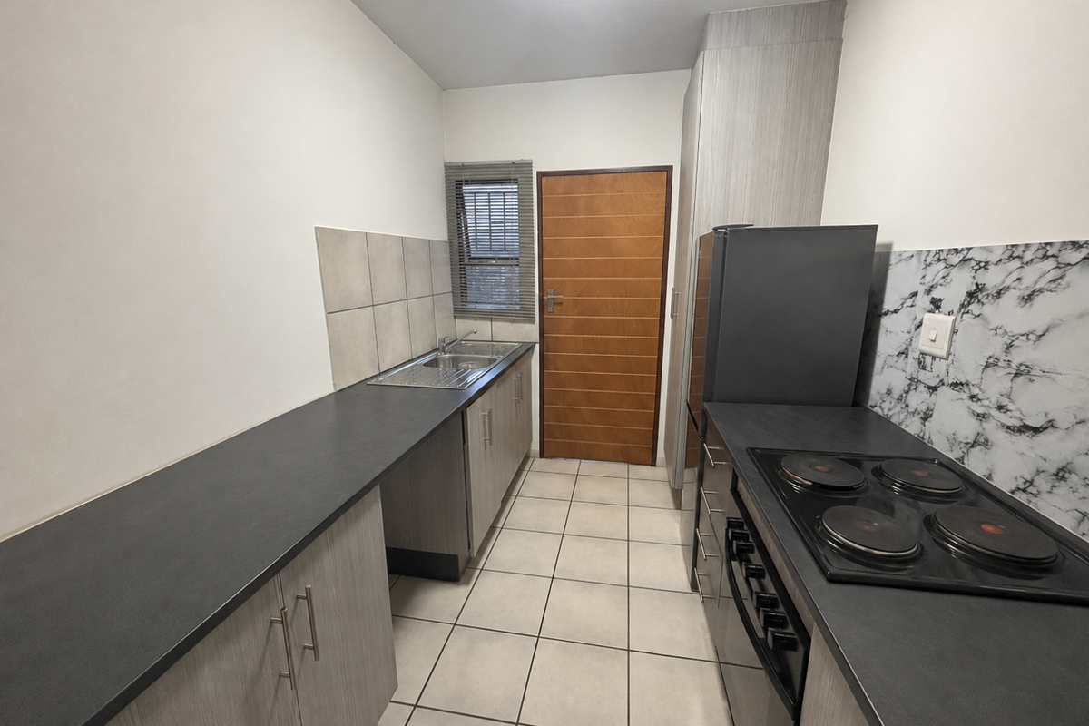 A functional galley-style kitchen featuring modern laminate countertops, built-in cabinetry, a stainless steel sink, and an integrated electric hob and oven.
