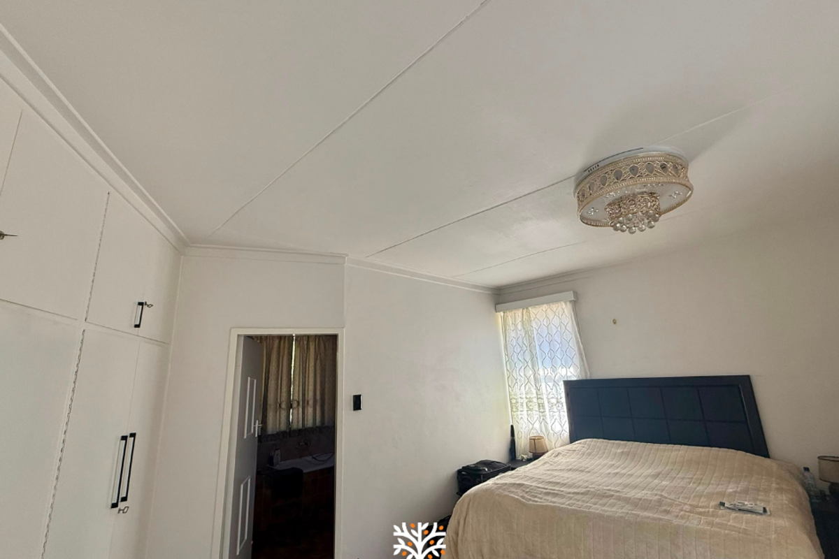 A bedroom featuring built-in cupboards and an en-suite bathroom access point, with neutral finishes and a decorative ceiling light fixture.