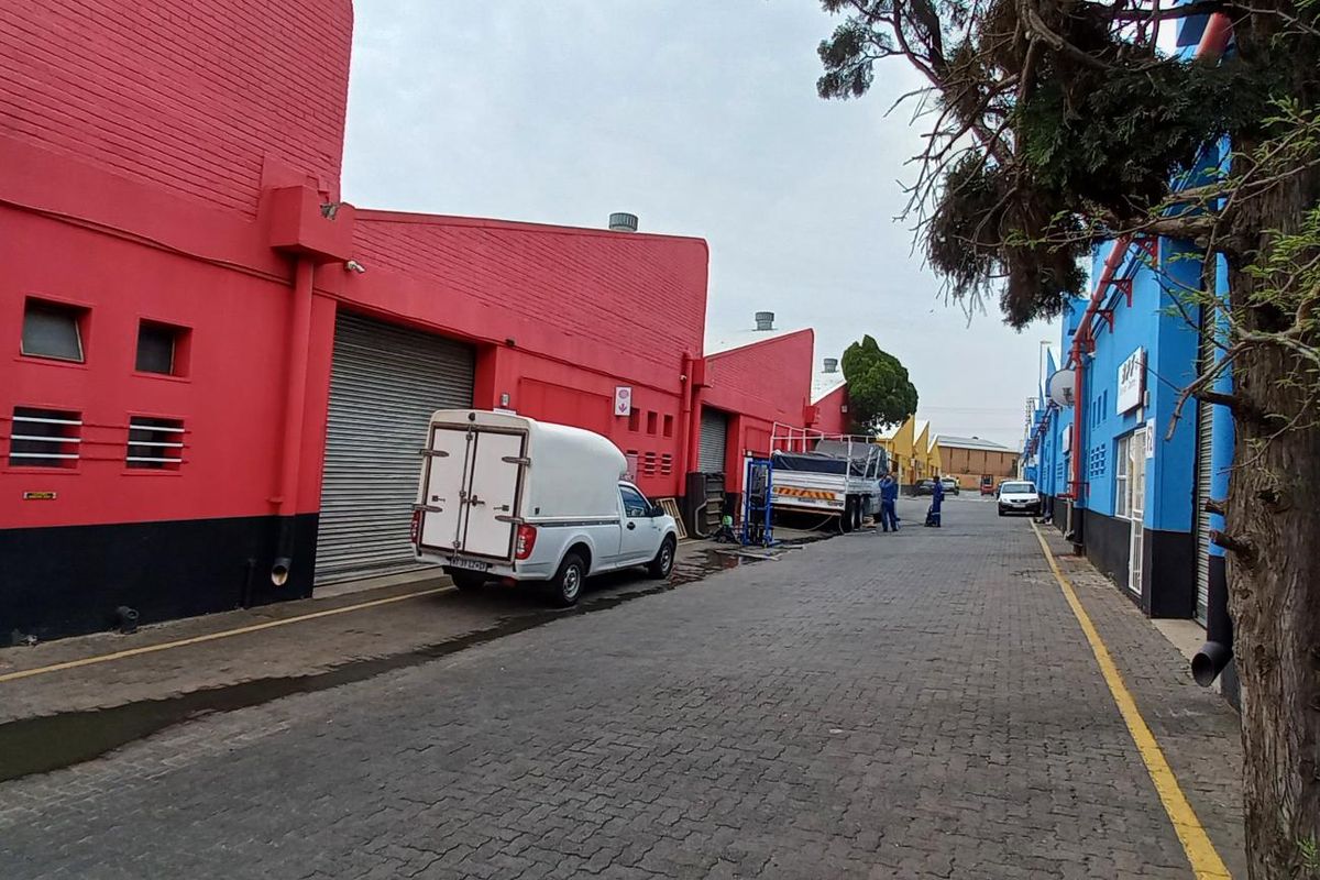Exterior view of an industrial complex featuring vibrant red and blue painted facades with roller shutter doors and a paved access road.