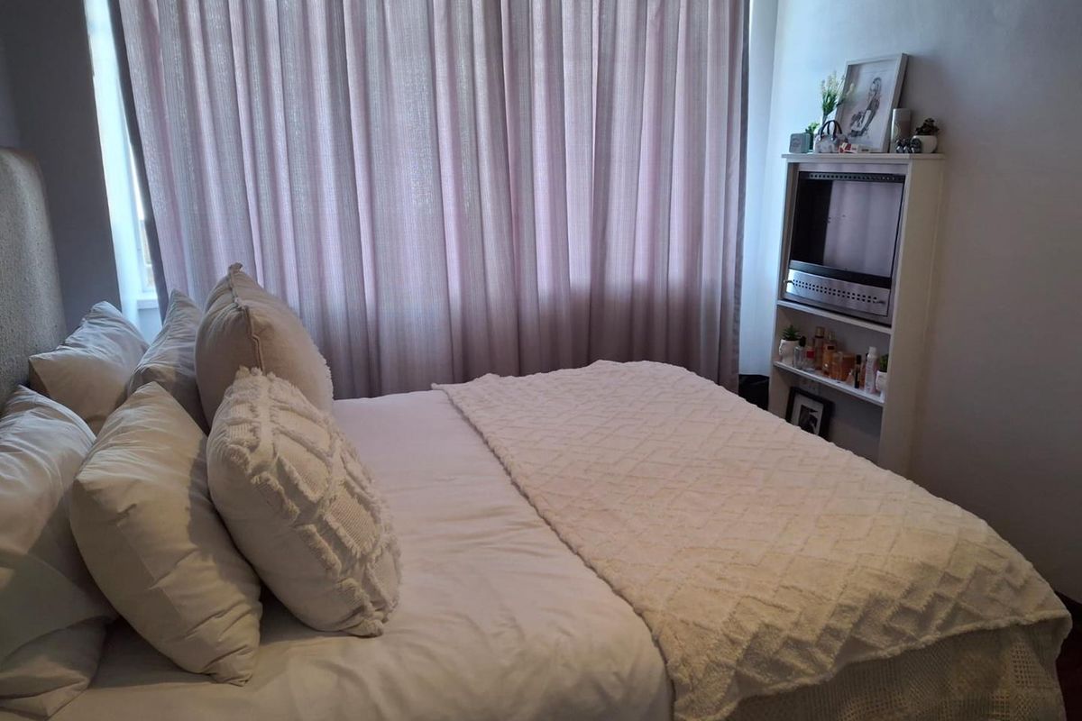A cozy bedroom featuring neutral tones, soft window drapery, and a built-in shelving unit, creating a comfortable and functional sleeping space.