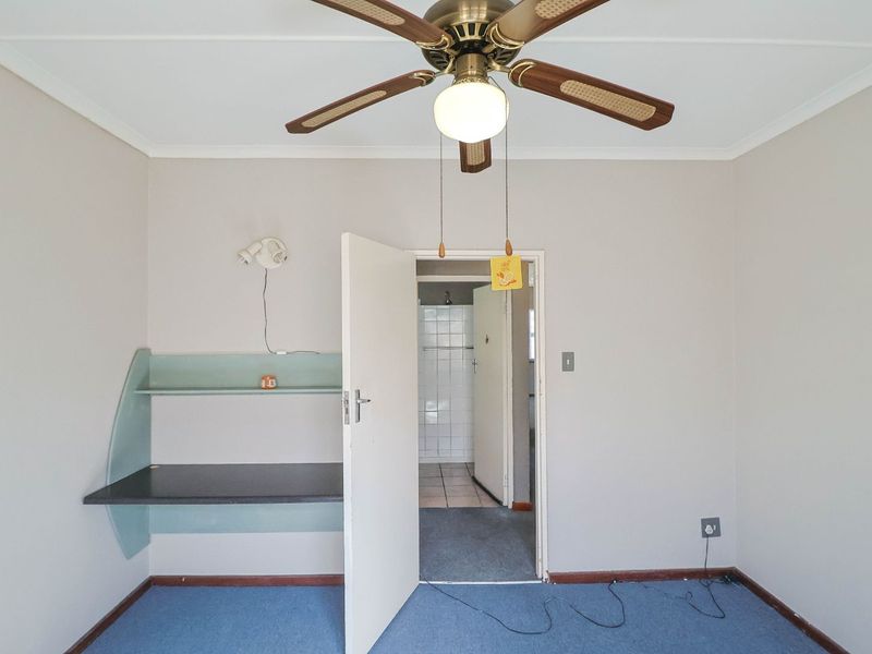 A vacant bedroom featuring a ceiling fan, built-in desk with shelving, and direct access to an en-suite bathroom.