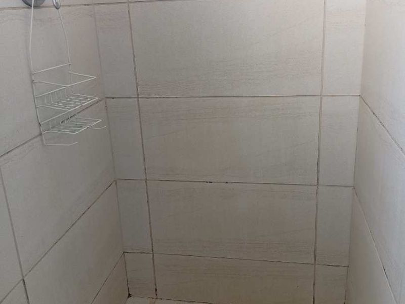 A shower enclosure featuring tiled walls and floor with a built-in mixer, showing signs of wear and grout discoloration.
