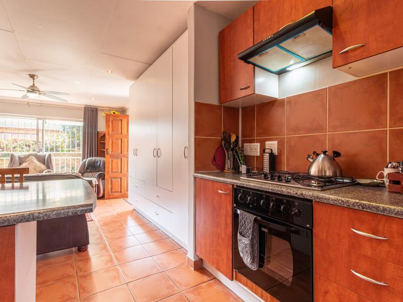 Open-plan kitchen and living area featuring wooden cabinetry, granite countertops, built-in oven and hob, tiled flooring, and access to an outdoor patio area.