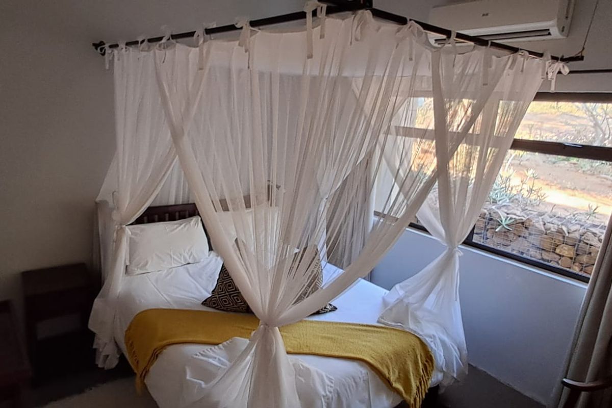 A cozy bedroom featuring a canopy bed, large windows with natural light, and a wall-mounted air conditioning unit.