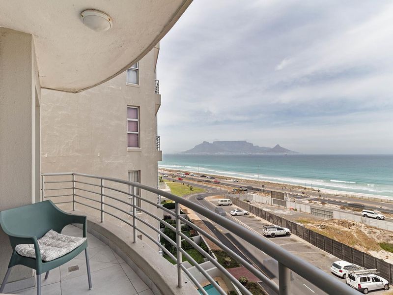 A curved balcony featuring tiled flooring and a metal railing, offering expansive views of the coastline and Table Mountain.