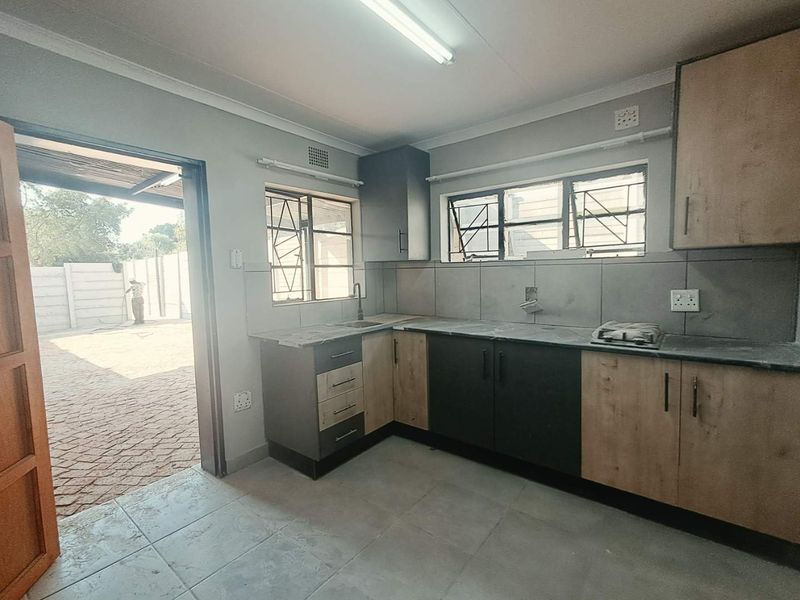 A functional kitchen featuring l-shaped cabinetry, laminate countertops, tiled backsplash, and direct access to an outdoor paved area.