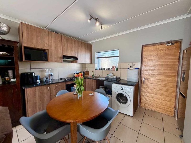 Functional kitchen featuring wood-look cabinetry, granite countertops, built-in oven, gas hob, and dedicated space for a washing machine with tiled flooring throughout.