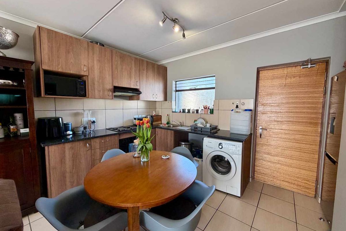 Functional kitchen featuring wood-look cabinetry, granite countertops, built-in oven, gas hob, and dedicated space for a washing machine with tiled flooring throughout.