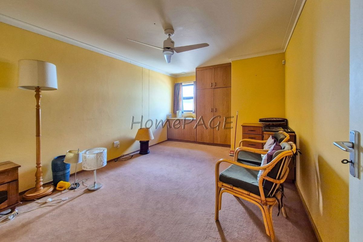 A bedroom featuring built-in wooden cupboards, a ceiling fan, and carpeted flooring, offering a functional space with potential for modernization.