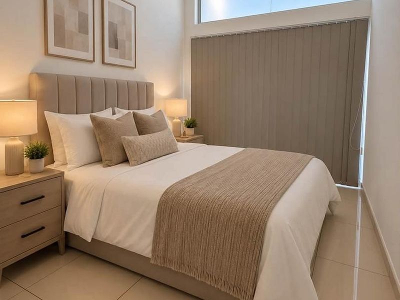 A well-maintained bedroom featuring neutral tiled flooring, a high-level clerestory window for natural light, and modern vertical blinds.