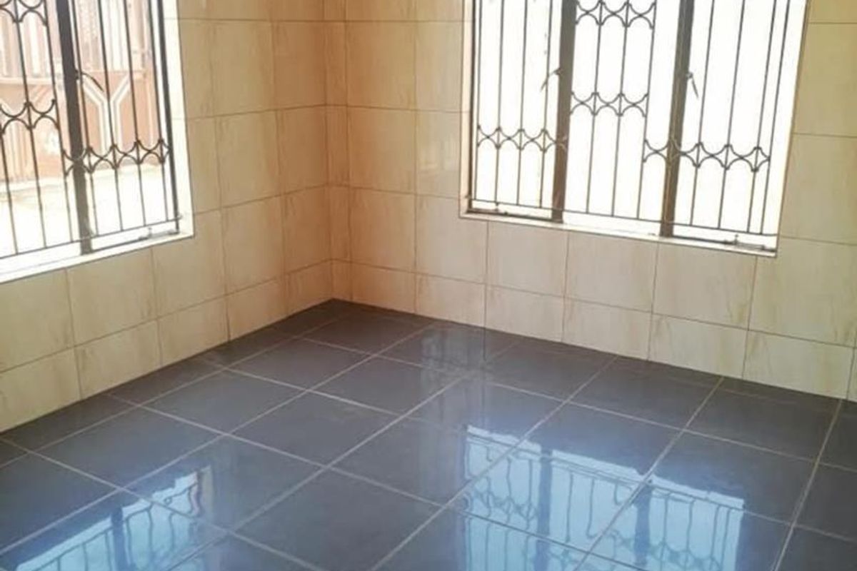 An empty living area featuring tiled flooring and wall tiling, complemented by windows fitted with security bars.