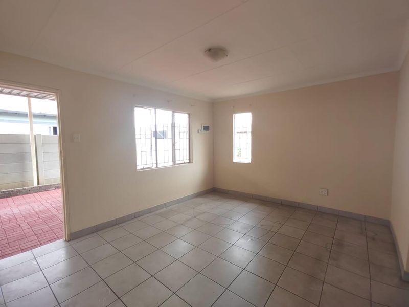 An empty living room featuring neutral tiled flooring, security bars on the windows, and direct access to an outdoor paved area.