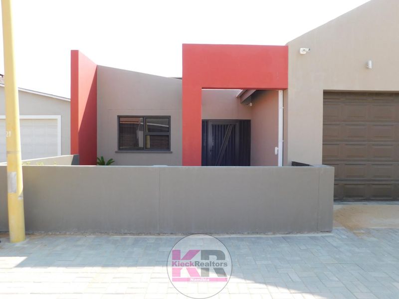 Modern front facade featuring a paved driveway, secure boundary wall, and a single garage with a sectional door.