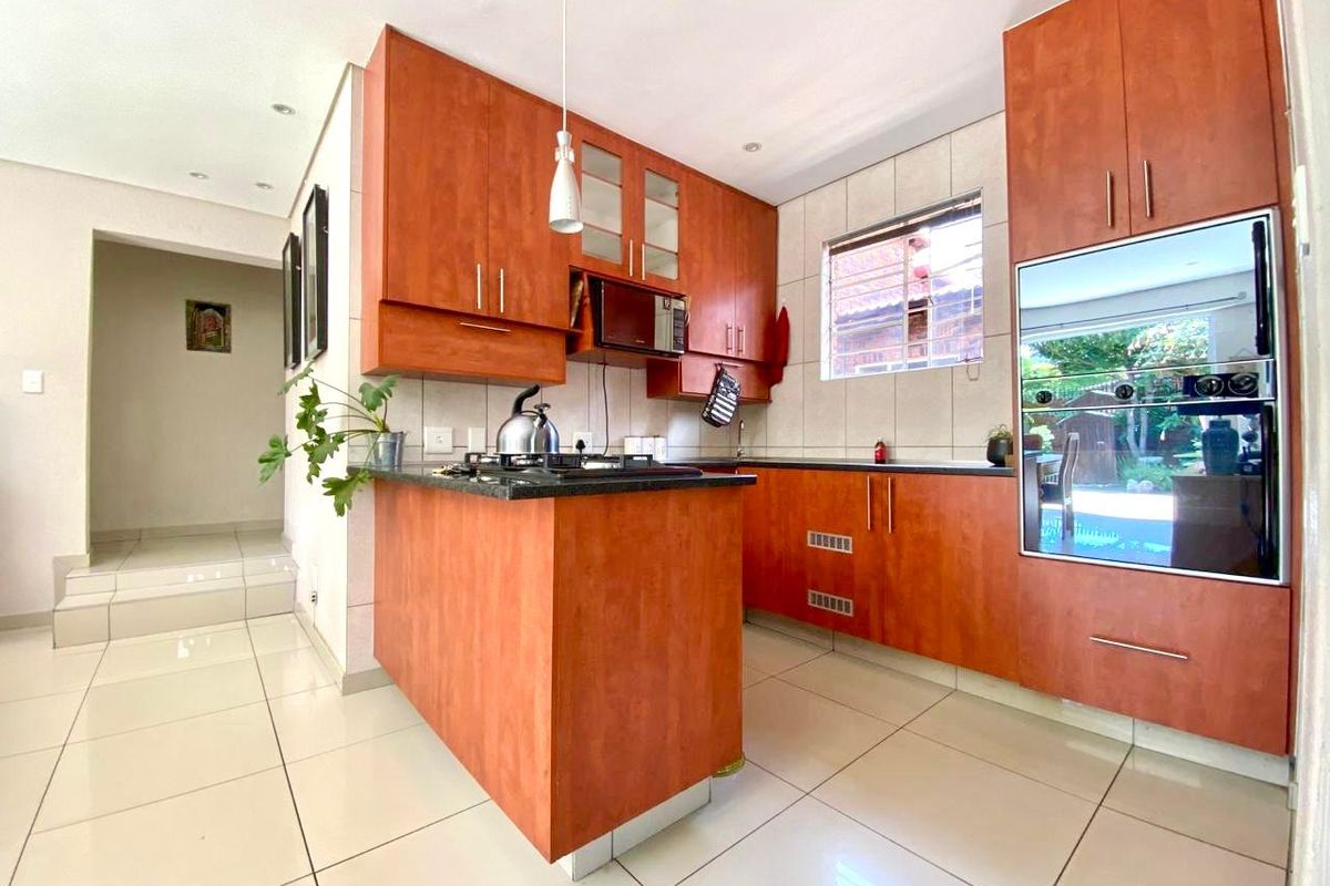 A functional kitchen featuring wood-finish cabinetry, granite countertops, a built-in oven, and tiled flooring, with a view through to the garden.
