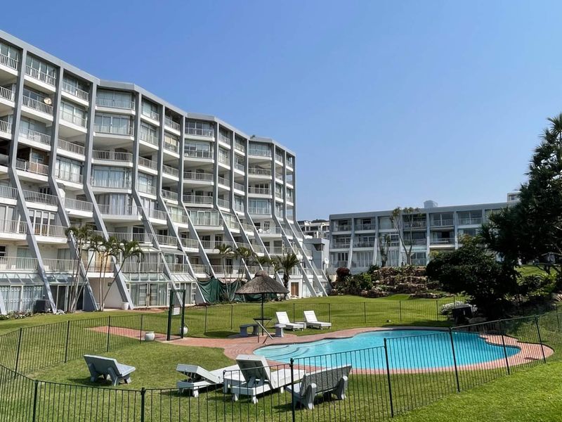 A view of the apartment complex exterior featuring a swimming pool, landscaped garden, and multiple levels of private balconies.