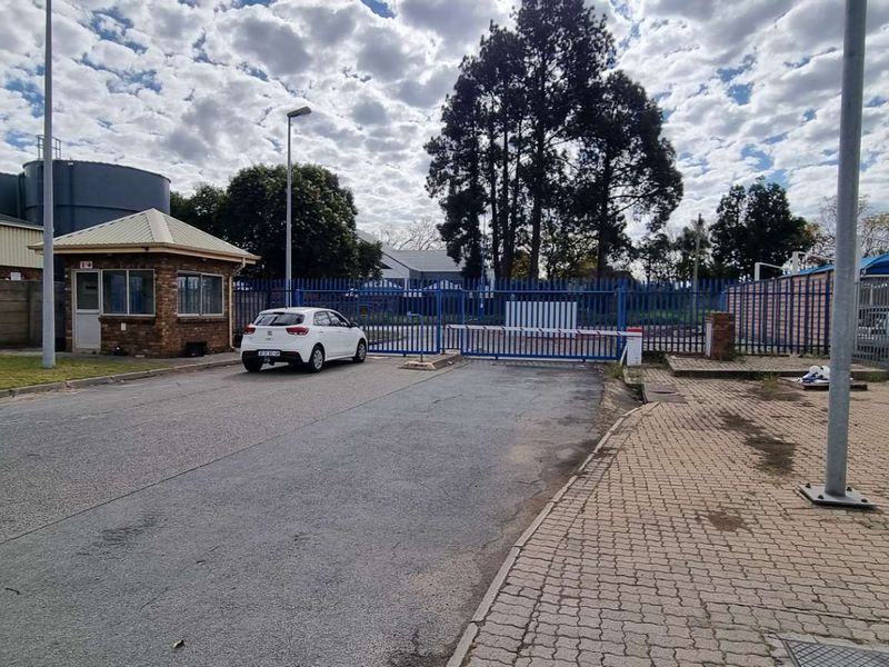 Commercial property entrance featuring a security guard house, paved driveway, and secure perimeter fencing with an automated boom gate access point.