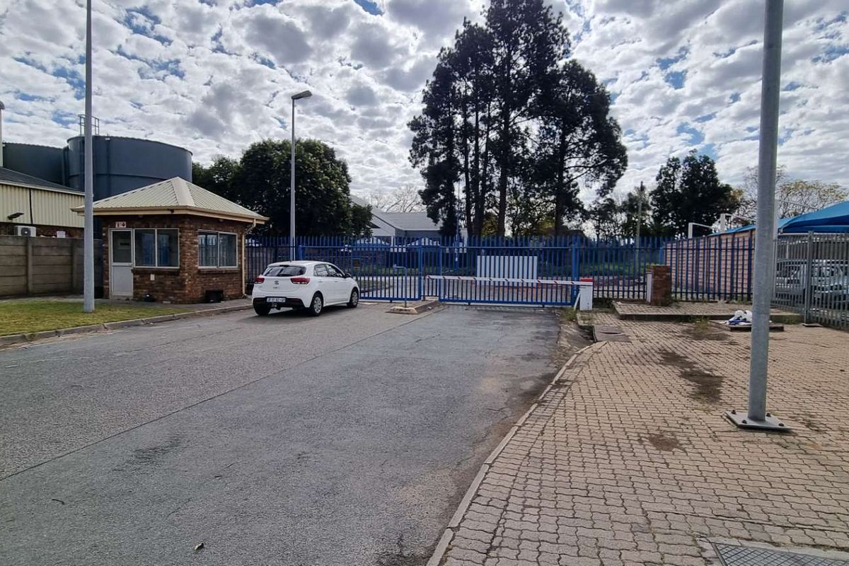 Commercial property entrance featuring a security guard house, paved driveway, and secure perimeter fencing with an automated boom gate access point.