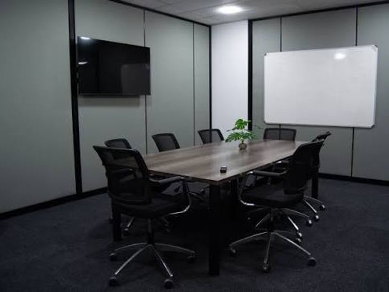 A professional office meeting room featuring partitioned walls, a wall-mounted whiteboard, a television, and recessed ceiling lighting.