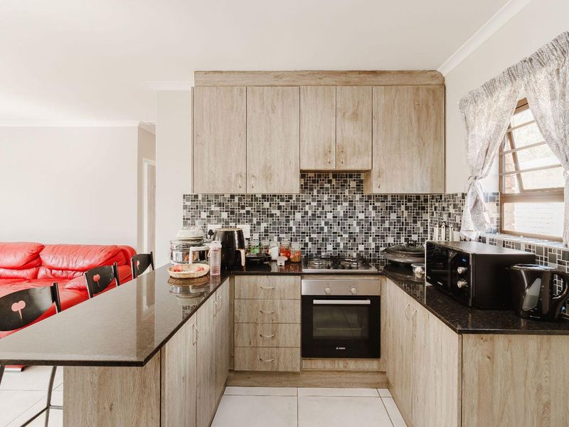 A functional kitchen featuring wood-look cabinetry, granite countertops, a mosaic tile backsplash, and integrated oven and gas hob.