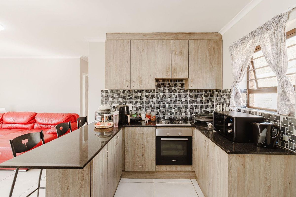 A functional kitchen featuring wood-look cabinetry, granite countertops, a mosaic tile backsplash, and integrated oven and gas hob.