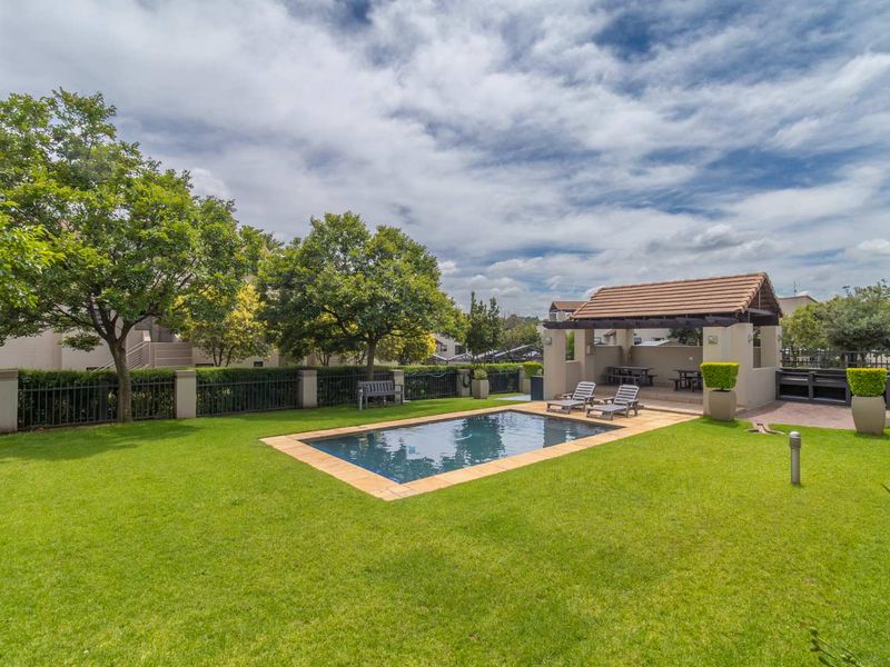 A well-maintained communal pool area featuring a swimming pool, manicured lawn, and a covered patio structure with tiled roofing.