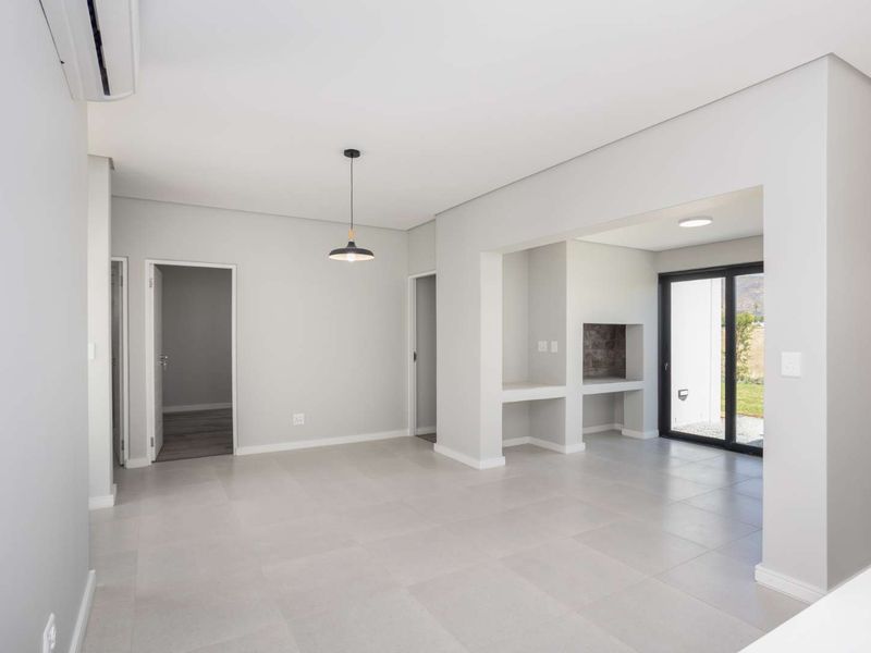 Spacious open-plan living area featuring neutral tiled flooring, a built-in braai, air conditioning, and direct access to the outdoor area through sliding glass doors.