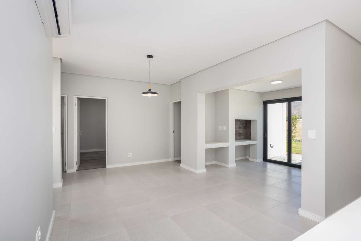 Spacious open-plan living area featuring neutral tiled flooring, a built-in braai, air conditioning, and direct access to the outdoor area through sliding glass doors.