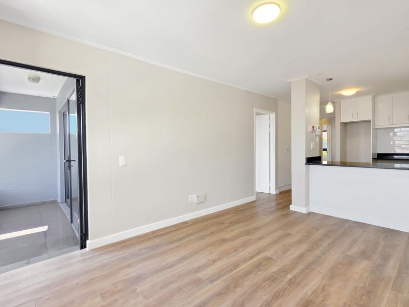 Bright open-plan living area featuring modern laminate flooring, neutral walls, and a functional kitchen with granite countertops and ample cabinetry.