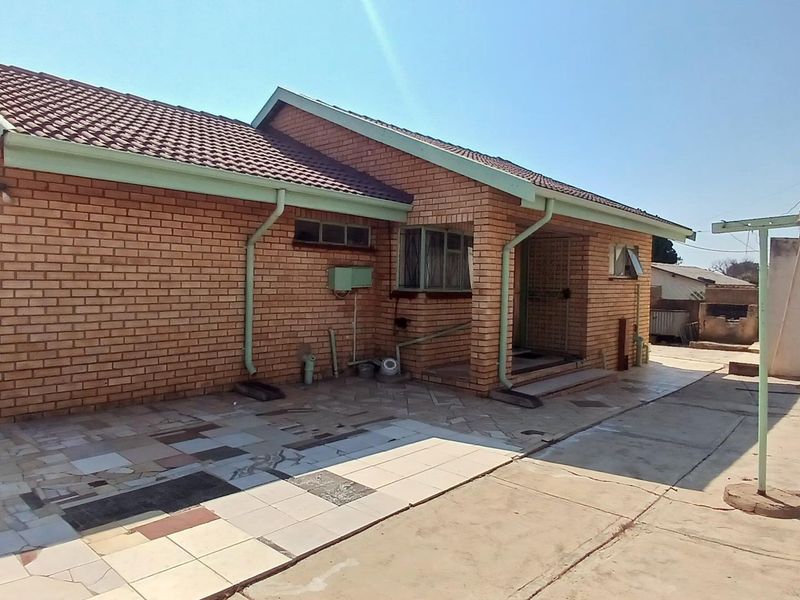Rear view of a brick house featuring a paved patio area, tiled roof, and an outdoor braai facility.
