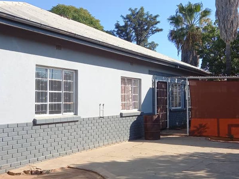 Rear view of the property featuring a concrete patio area, brick and plaster facade, and security-barred windows.