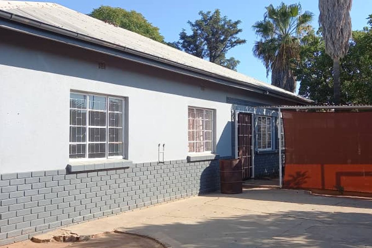 Rear view of the property featuring a concrete patio area, brick and plaster facade, and security-barred windows.