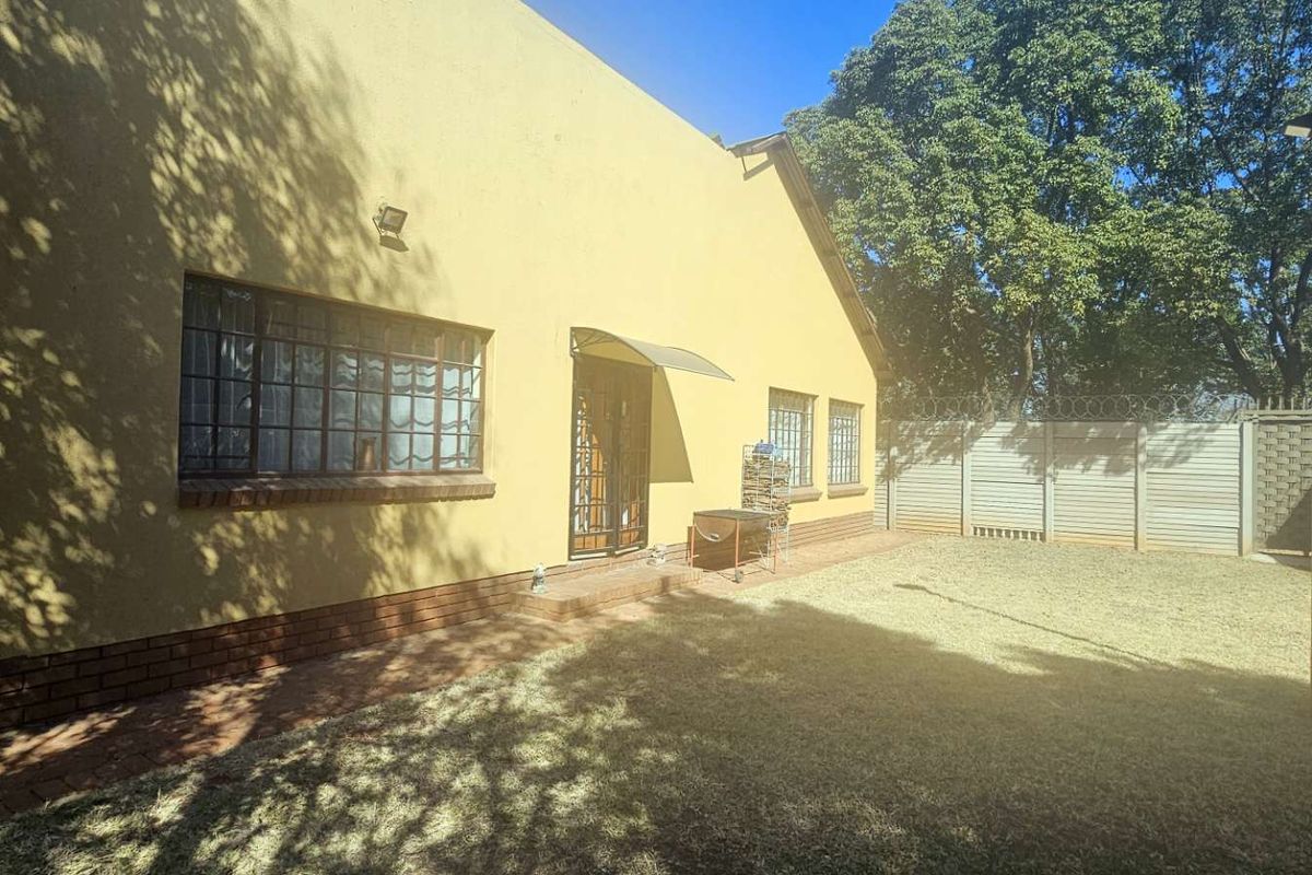Rear view of the property featuring a private garden, paved walkway, and secure perimeter walling with razor wire.