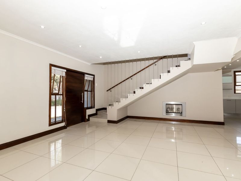 Spacious open-plan living area featuring polished tile flooring, a modern staircase with metal balustrades, and a built-in fireplace.