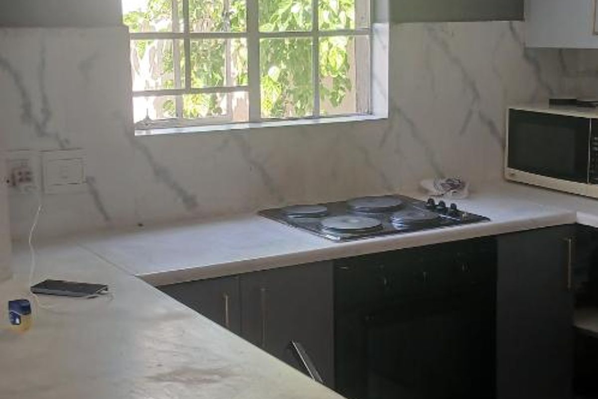 A functional kitchen featuring a built-in oven, electric hob, marble-look splashback, and tiled flooring, offering a practical layout with a breakfast bar area.