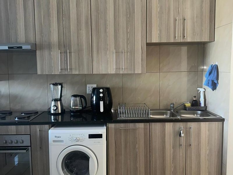 A functional kitchen featuring wood-look cabinetry, granite countertops, a built-in oven with hob, and integrated space for a washing machine.