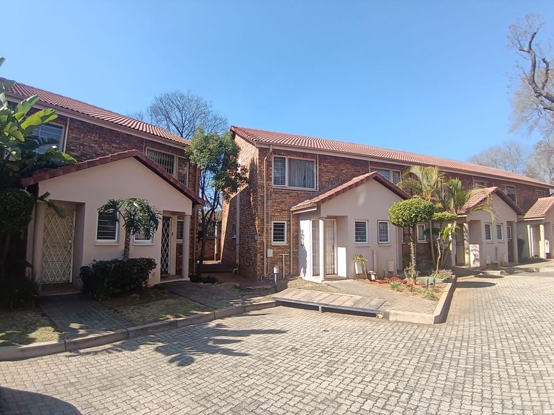 Exterior view of a residential apartment complex featuring brick facades, tiled roofs, and paved driveway access with established garden beds.