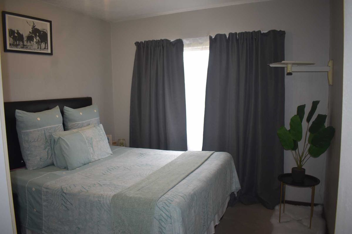 A cozy bedroom featuring neutral wall tones, a window with curtain treatments, and carpeted flooring.