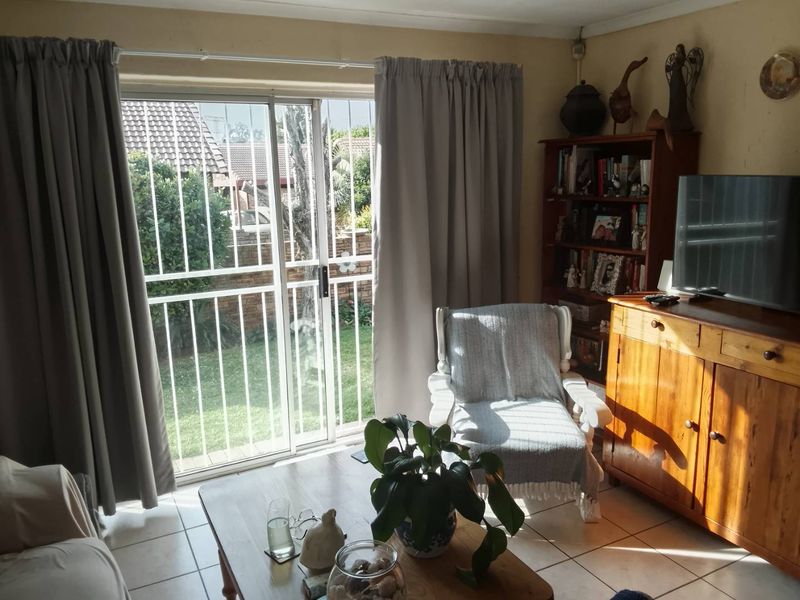 A living room featuring tiled flooring and a sliding glass door with a security gate, providing direct access to the garden area.