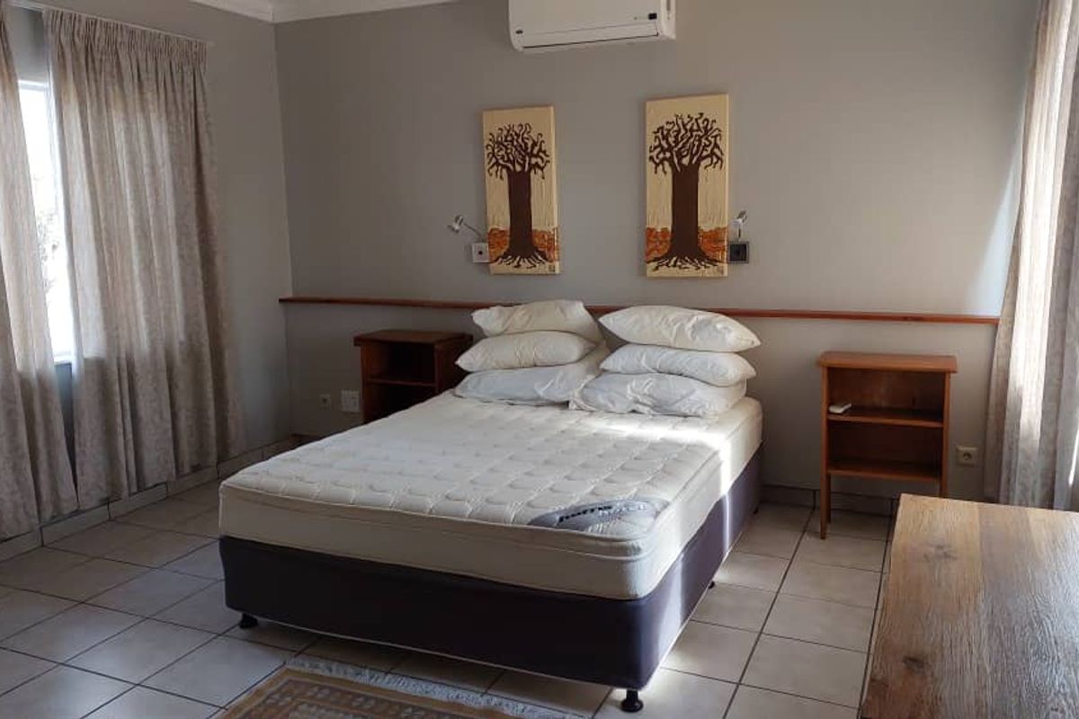 A spacious bedroom featuring tiled flooring, a wall-mounted air conditioning unit, and dual bedside shelving units.