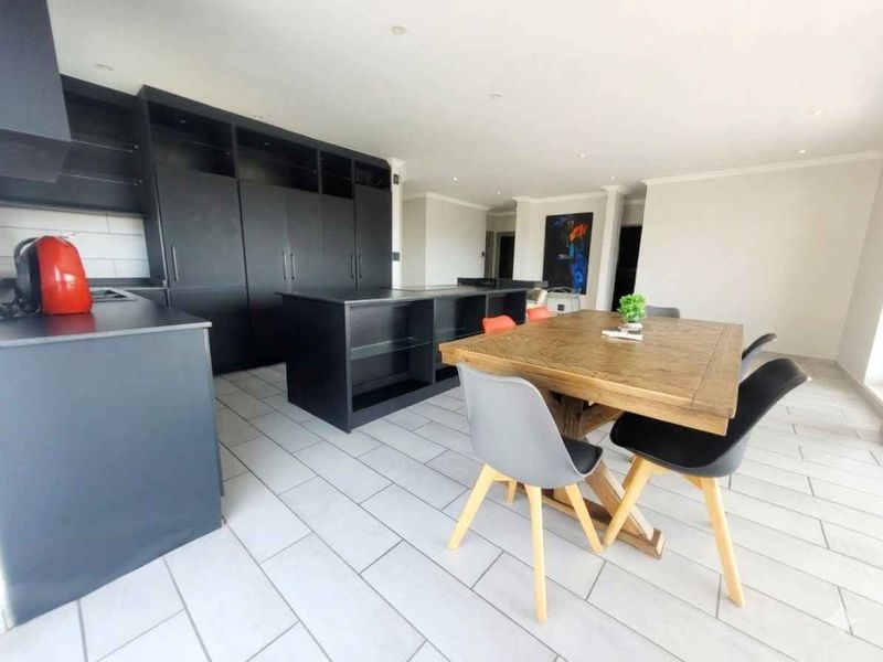 Modern open-plan living area featuring sleek black built-in cabinetry, a central kitchen island, and light-toned tiled flooring throughout the space.