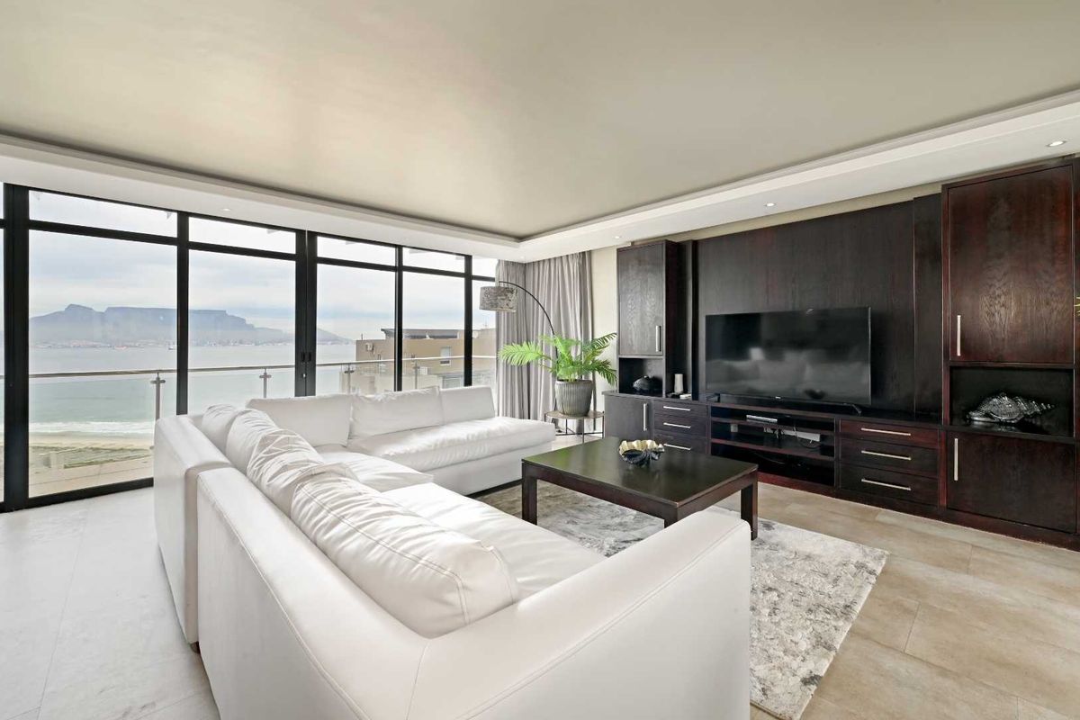 Spacious living area featuring floor-to-ceiling windows with panoramic ocean and mountain views, complemented by custom dark wood built-in cabinetry and tiled flooring.