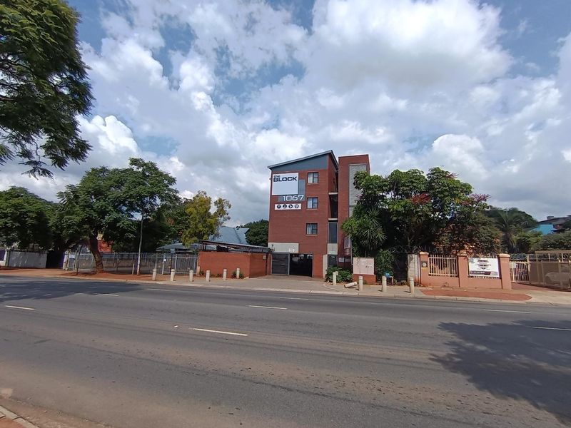 Street-facing view of The Block apartment complex, featuring a multi-story brick facade, secure perimeter fencing, and paved access.
