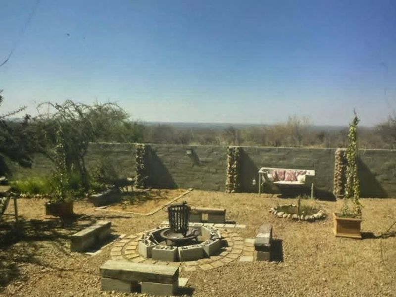 A rustic outdoor garden area featuring a central built-in fire pit, gravel landscaping, and a stone boundary wall with expansive landscape views.